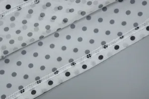 Close-up of black polka dot print on white mesh fabric showing fine stitching detail