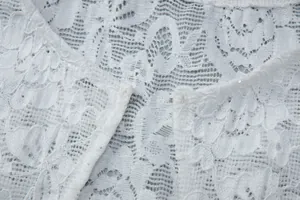 Detailed view of elegant white floral lace fabric with sequins and hook closure