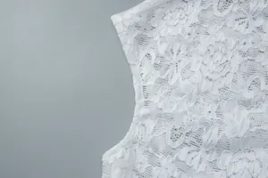 Close-up of white floral lace fabric with delicate sequin accents on a stylish top