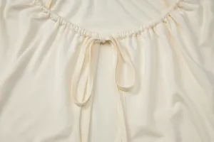 Close-up of a cream women's top with gathered neckline and adjustable tie detail