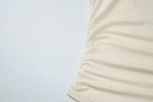 Close-up macro detail showing the side ruched gathering on a cream minimalist women's T-shirt