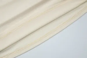 Close-up detail showing the neat double-stitch hem on soft cream knit fabric for women's top