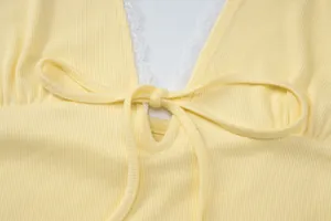 Close-up detail of yellow ribbed knit top with white lace trim and adjustable front tie knot