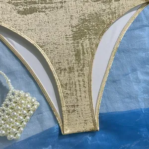Macro detail of a shimmering gold metallic textured swimsuit fabric with pearl accessory props
