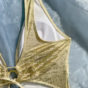 Close-up detail of golden metallic finish fabric and ring hardware on a sexy swimsuit