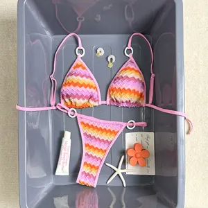 Detailed flat lay of a colorful pink gradient zigzag bikini set with beach vacation props