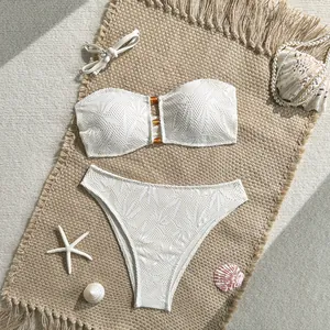 Set bikini a fascia in pizzo bianco con dettaglio di perle decorative su stuoia da mare.