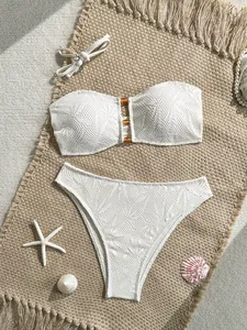 Dettaglio di un set bikini in pizzo bianco con accenti in ambra e slip a vita alta.