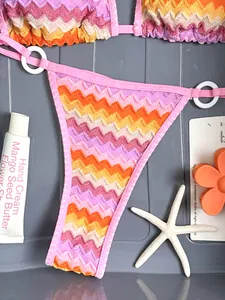 Detailed view of colorful zigzag stripe bikini with summer beach props on gray background.