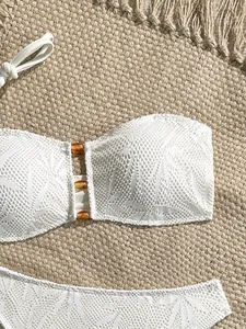 Dettaglio di un top bikini in pizzo bianco con accenti di perline ambra e rete floreale