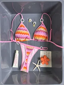 Close-up of pink zigzag striped bikini set with summer accessories in a gray tray