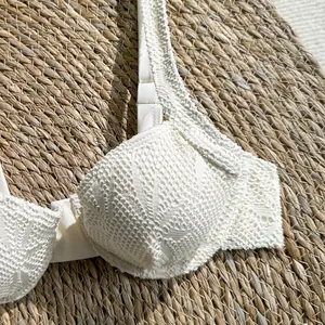 Close-up macro view of a white hollow-out lace bikini top with delicate crochet patterns.