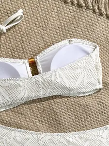 Primo piano di un top bikini in pizzo bianco con dettaglio anello centrale in resina. (83 chars)