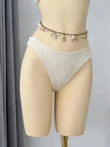 Detail van wit gehaakt bikinibroekje met decoratieve schelpen tailleketting