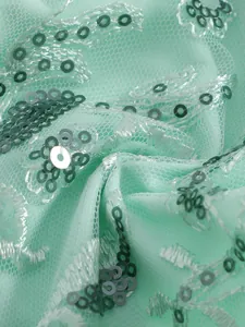 Macro detail of mint green swimwear fabric featuring delicate lace and shiny silver sequins