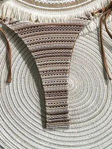 Detailed view of the striped crochet bikini bottom against a boho woven beach mat backdrop