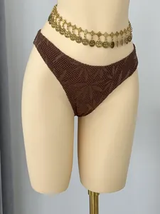 Detail van bruin gehaakt bikinibroekje met een decoratieve goudkleurige heupketting