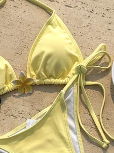 Gedetailleerde weergave van gele halterbikini-set met een decoratieve plumeriabloem