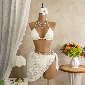 Detailed view of white crochet three-piece bikini set with lace skirt and shell decor