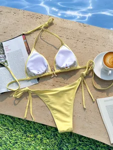 Detailweergave van de gele halterbikiniset met gouden vlinderbedel aan het zwembad