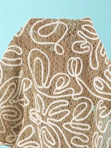 Macro detail of tan crochet beach cover-up with white wavy embroidery and mesh texture