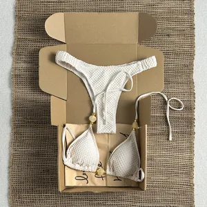 White textured bikini set with yellow beaded detail inside a kraft packaging box