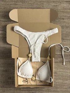 Close-up of white textured bikini set with decorative amber beads in a gift box.