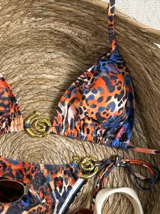 Détail du bikini imprimé léopard avec anneaux métalliques dorés dans un panier en paille.