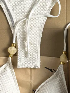 Detailed macro shot of white textured bikini set featuring gold and marble bead accents