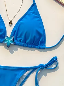 Detail van een felblauwe bikinitop met een decoratieve bloemvormige bedel en veters.