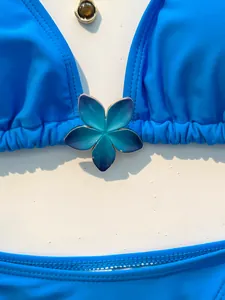 Detailweergave van een helderblauwe bikinitop met een centraal blauw bloemornament.