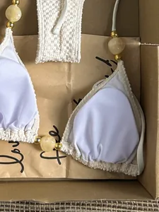Close-up detail of a white halter bikini top with amber bead accents in a gift box packaging