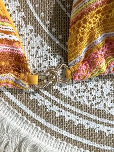 Detailed macro shot of a colorful crocheted bikini top with a golden heart-shaped clasp.