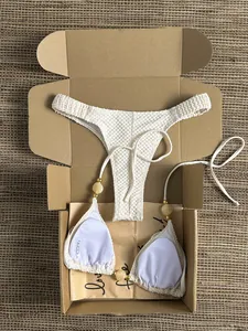 Close-up of white crinkle bikini set with gold bead details in gift box packaging