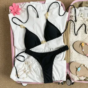 Black halter bikini set with beaded details shown inside a pink vacation suitcase.