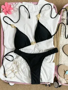 Black textured halter bikini set with decorative beads laid in a pink travel suitcase.