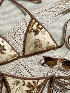 Detalle de un bikini crema con bordado floral de lentejuelas doradas y borde marrón