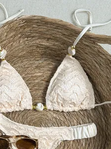 Gedetailleerde close-up van een crèmekleurige kant bikini met marmeren en gouden kralen.