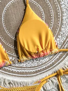 Detail of yellow bikini top featuring colorful crochet edges and gold-tone metal connector