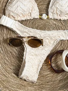 Detailopname van een crème kanten bikini met kralendetails op een geweven rieten mat.
