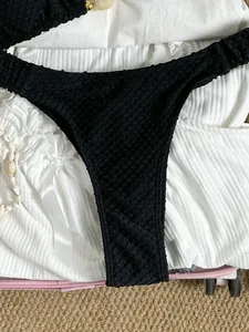 Close-up detail of black textured bikini bottom laid on white vacation dress fabric