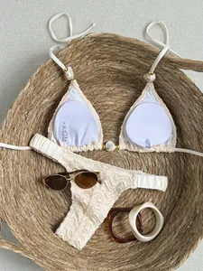 Gedetailleerde opname van een crème getextureerde bikini met kralen en kant details