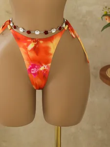 Detailopname van een bohemien bloemen bikini-broekje met rozen en kristallen ketting