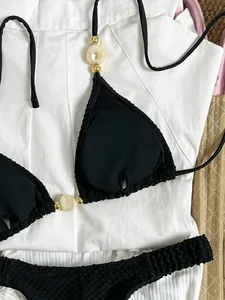 Close-up detail of black bikini top featuring elegant marble beads and textured ribbed fabric.