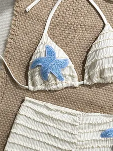 Gros plan d'un bikini crème texturé avec des patchs d'étoiles de mer en paillettes bleues.