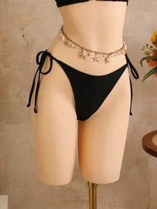 Detailopname van een goudkleurige tailleketting met schelpen en zeesterren voor het strand.