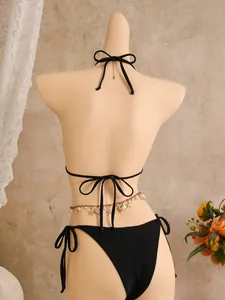 Detailweergave van de achterkant van een zwarte bikini met schelp- en pareltailleketting