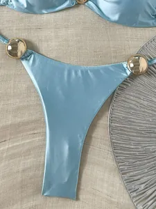 Detailansicht der hellblauen glänzenden Bikinihose mit goldenen Metallringen.