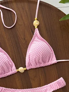 Textured pink halter bikini detail with marble-style cream and gold bead accents.
