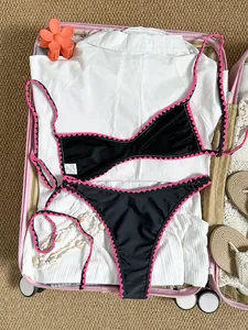Lifestyle-Ansicht eines schwarzen Bikinis mit rosa Häkelborte in einem rosa Koffer